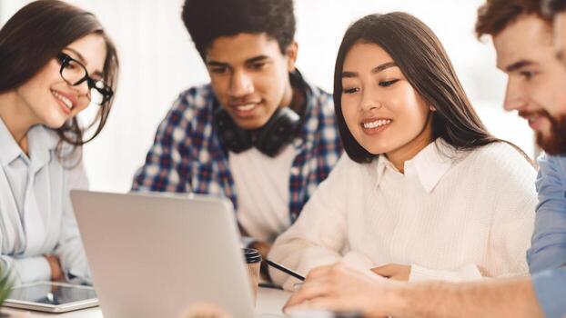Multiethnic students leverage technology for learning in the library, each absorbed in their device. The setting is serene, promoting a studious atmosphere. photo
