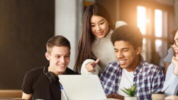A diverse group of students are gathered around a laptop, attentively looking at the screen. They appear to be engaged in a discussion or viewing content together. photo