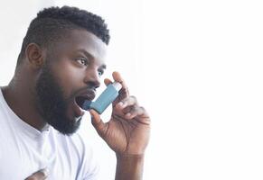 Young african man using asthma inhaler at home. Modern generation sickness, empty space photo
