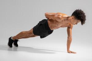A young man demonstrates an advanced push-up technique, showcasing strength and control. He focuses on proper form while balancing on one hand, contributing to his upper body workout photo