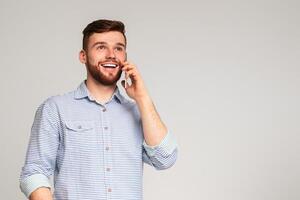 Great news. Cheerful man using his phone have conversation and widely smiling on studio background, free space photo