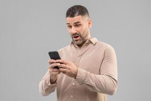 Surprised man with short hair holding a smartphone in his hand, looking down at the screen. He appears focused on using the device. photo
