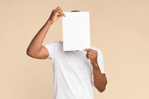 Unrecognizable African American Man Covering Face With White Paper Standing Over Yellow Background. Mockup, Studio Shot photo