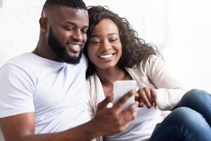 A happy couple sits together looking at a smartphone. They are both smiling, suggesting that they are enjoying their time together. photo