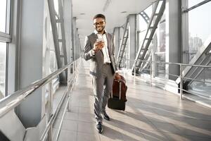 A professional black man is on his phone with baggage in an airport. The atmosphere is lively and efficient, reflecting the pace of modern business travel. photo