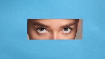 A close-up of a woman eyes with a neutral expression, set against a solid blue background. The woman features are in focus, showing fine details like her eyes, nose photo