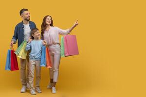 A man and a woman stand holding shopping bags while next to a child, surrounded by a shopping environment. The trio appears to be engaged in a family outing or shopping trip, copy space photo
