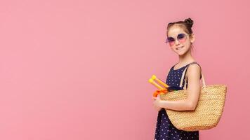 On way to beach. Little girl going to swim with diving mask in wicker bag, pink studio background photo