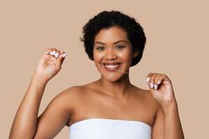 A young woman stands against a soft beige backdrop, smiling as she demonstrates proper dental floss usage with a length of floss between her fingers photo