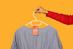A person is holding a shirt on a hanger, showcasing the price tag attached to it. The shirt appears neatly displayed and ready for purchase, cropped photo