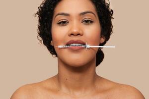 Half-naked woman is shown with a syringe held between her lips. She appears to be preparing for an injection or taking medication orally. photo