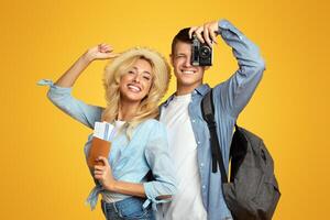 Ready for vacation. Cheerful young couple with suitcase and tickets posing over yellow background, copy space photo
