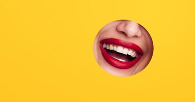Laughing woman mouth is visible as she peers through a round hole in a vibrant yellow background. The lips are painted red, adding a striking contrast to the bright backdrop. photo