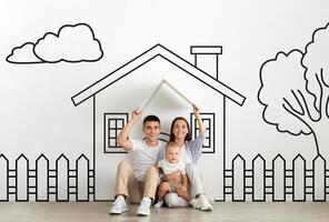A family composed of parents and little baby is seated on the floor in front of a detailed drawing of a house. They seem engaged in discussing or admiring the artwork together in a home environment. photo