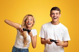 Gambling young couple playing game with joysticks, yellow studio background with copy space photo