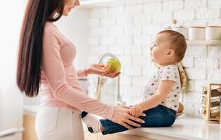A woman is gently holding an apple towards a baby, who is reaching out to touch the fruit. The baby appears curious and excited, while the woman seems caring and affectionate. photo