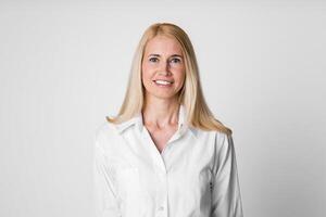 A smiling woman with blonde hair and wearing a white button-down shirt stands against a white background. Her bright white shirt has a collar and long sleeves photo