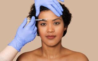 A woman is undergoing filler injection on her forehead. A healthcare professional is carefully administering the injection to reduce wrinkles and fine lines, closeup photo