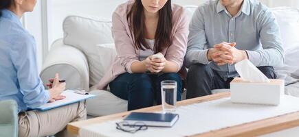 Cropped of couple is seated on a sofa during a counseling session with a therapist. They appear to be engaged in discussion, with the therapist taking notes photo