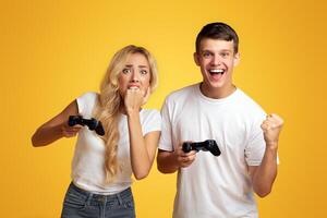 Gambling young couple playing game with joysticks, yellow studio background with empty space photo
