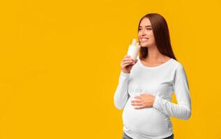 Cheerful Pregnant Lady Drinking Natural Milk Touching Belly And Smiling Standing On Pink Studio Background. Free Space photo