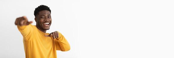 Funny charismatic handsome african american millennial guy in yellow sweater gesturing while posing on white studio background and smiling, pointing with index fingers, copy space photo