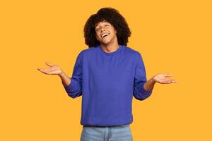 The man expresses joy with a wide smile, raising both hands in an open gesture as if inviting interaction. Wearing a casual blue sweater and displaying curly hair photo