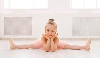 Little ballerina in split on floor, copy space. Smiling baby girl dreaming to become professional ballet dancer, classical dance school photo