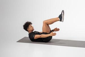 A young man engages in a core strengthening exercise on a mat, focusing on his form and technique. The indoor setting is bright and minimalistic, emphasizing his workout photo