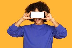 Guy is holding a cell phone with white blank screen up to his face, possibly making a call or taking a selfie. The individuals hand is visible and the focus is on the phone screen. photo
