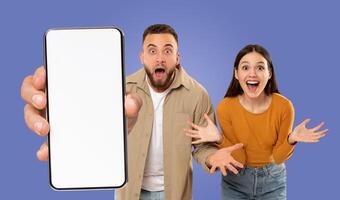 A young man and woman stand in front of a purple background, holding a smartphone with a blank white screen, showing nice mobile app or online offer photo