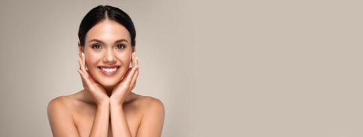 Cheerful young woman posing topless over grey studio background, touching her face and smiling, copy space photo