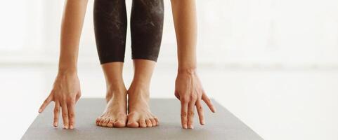 Lady is engaged in a yoga session indoors during the daytime, bending forward to touch their toes on a yoga mat, emphasizing flexibility and concentration, panorama with copy space photo