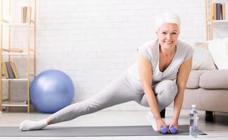 Active senior woman warming up, doing legs stretching exercises at home, panorama with empty space photo