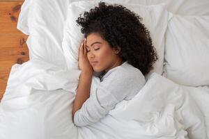 Pretty Hispanic woman is laying down on a bed, her head cradled in her hands. She appears to be deep in thought or contemplation, with a sense of introspection and reflection evident in her posture. photo