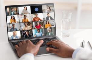 A persons hands are visible typing on a laptop while a virtual meeting with several participants is displayed on the screen. Experience of virtual communication, collaboration in the modern workplace. photo