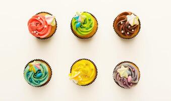 Top view on set of vanilla cupcakes with colorful buttercream tops isolated on white background. Tasty desserts in brown muffin liners. Delicious treats for birthday party, bakery concept, cutout photo