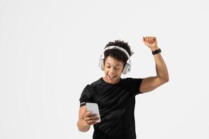 A young guy is joyfully dancing while listening to music through headphones, holding a smartphone in one hand. The vibrant expression and movement indicate enjoyment photo