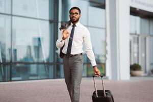 Black man business traveler is at the entrance of a modern airport. The mood is energetic and professional, with a focus on travel and business amidst a sleek airport background. photo