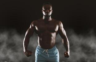 A muscular man stands with his fists clenched, posing in front of a dark background with smoke. photo