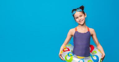 A young girl wearing a blue and white striped swimsuit is seen holding a large inflatable float. She appears to be enjoying a day at the pool or beach, copy space photo