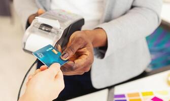 African American lady holding a credit card in her hand, showing the front side with a chip and embossed numbers. The background is a simple, neutral color to give focus to the card. photo