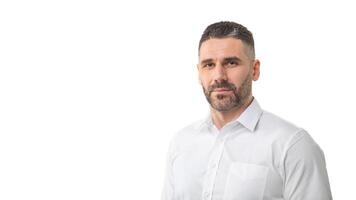 A man with a short beard and trimmed hair is standing against a plain white background, wearing a white button-up shirt. He has a neutral expression, panorama with copy space photo