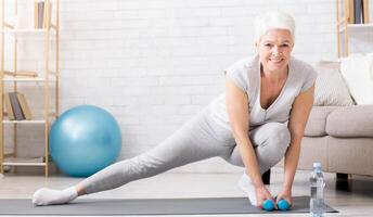 Active senior woman warming up, doing legs stretching exercises at home, panorama with empty space photo