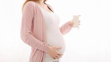 A pregnant woman, with a noticeable baby bump, is standing while holding a glass of milk in her hand, showcasing the healthy beverage choice she is making during her pregnancy, cropped photo