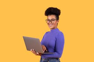 A young woman stands confidently while using a laptop, displaying a joyful expression. She wears a stylish purple top and has her hair in natural curls, creating a vibrant and engaging atmosphere photo