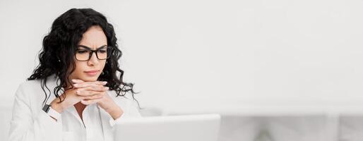 Problem Solving. Focused mexican businesswoman working on laptop at office, thinking about difficult task, copyspace photo