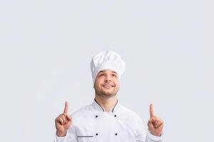 Look Up. Positive Chef Guy Pointing Fingers Upward Standing Over White Studio Background. Panorama photo