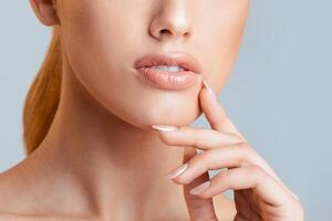 This image shows a close-up of a woman face and hand against a light blue background. The image focuses on the woman lips, chin, and hand resting on her cheek, cropped photo