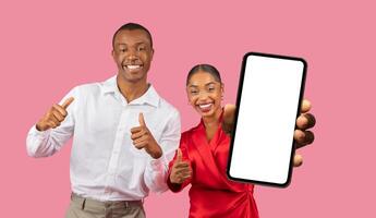 This image features a happy African American couple standing in front of a pink background. The woman is holding a smartphone with a blank screen in front of her, while the man is giving a thumbs-up photo
